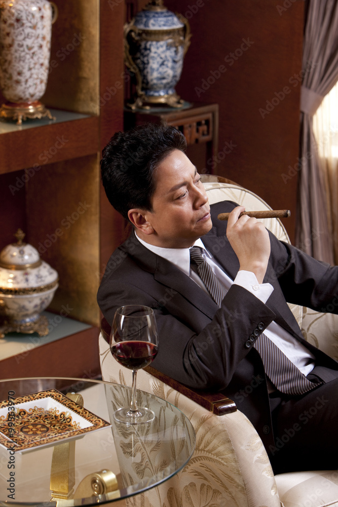 成熟的商人在豪华的房间里享受雪茄和葡萄酒