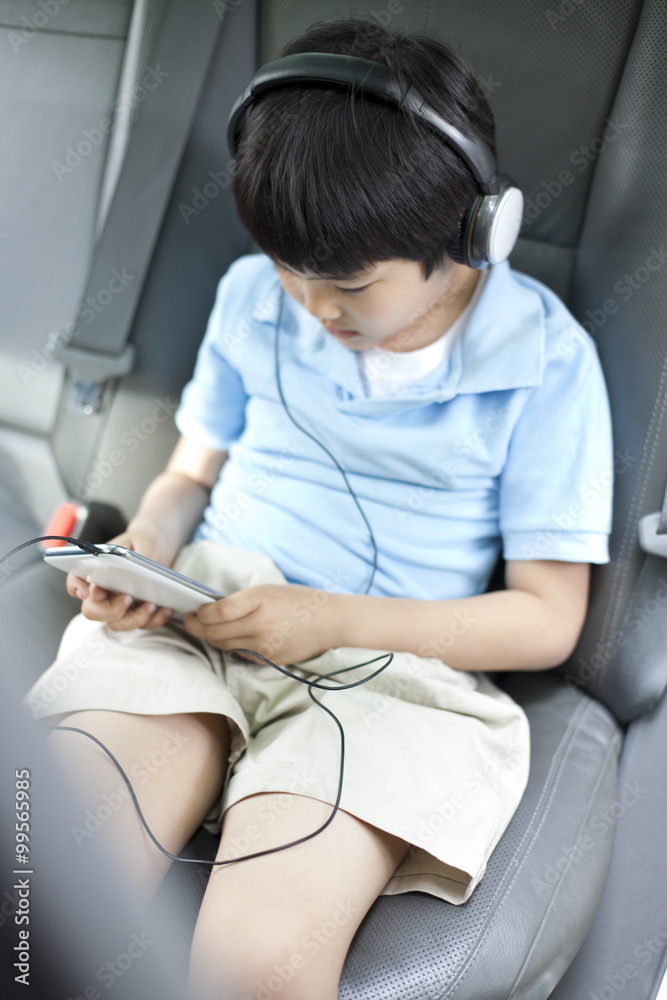 可爱的男孩在车里用智能手机听音乐