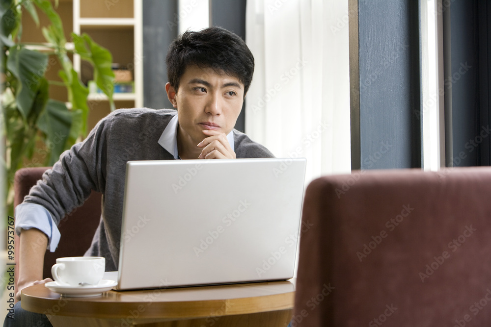一个男人在咖啡店的笔记本电脑前思考