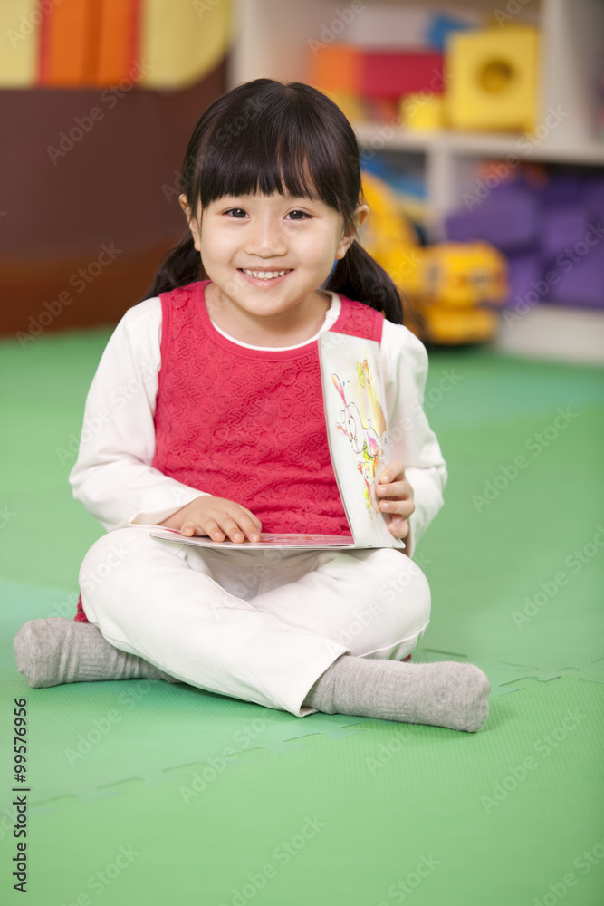 可爱的小女孩坐在地板上，手里拿着书