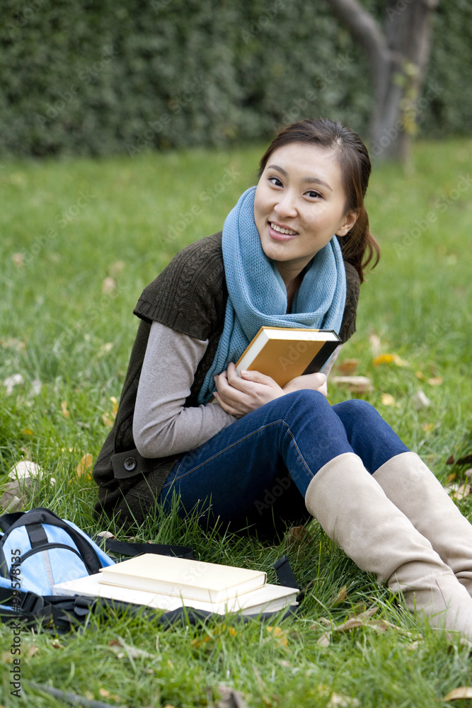 一位年轻女子坐在草地上拿着一本书