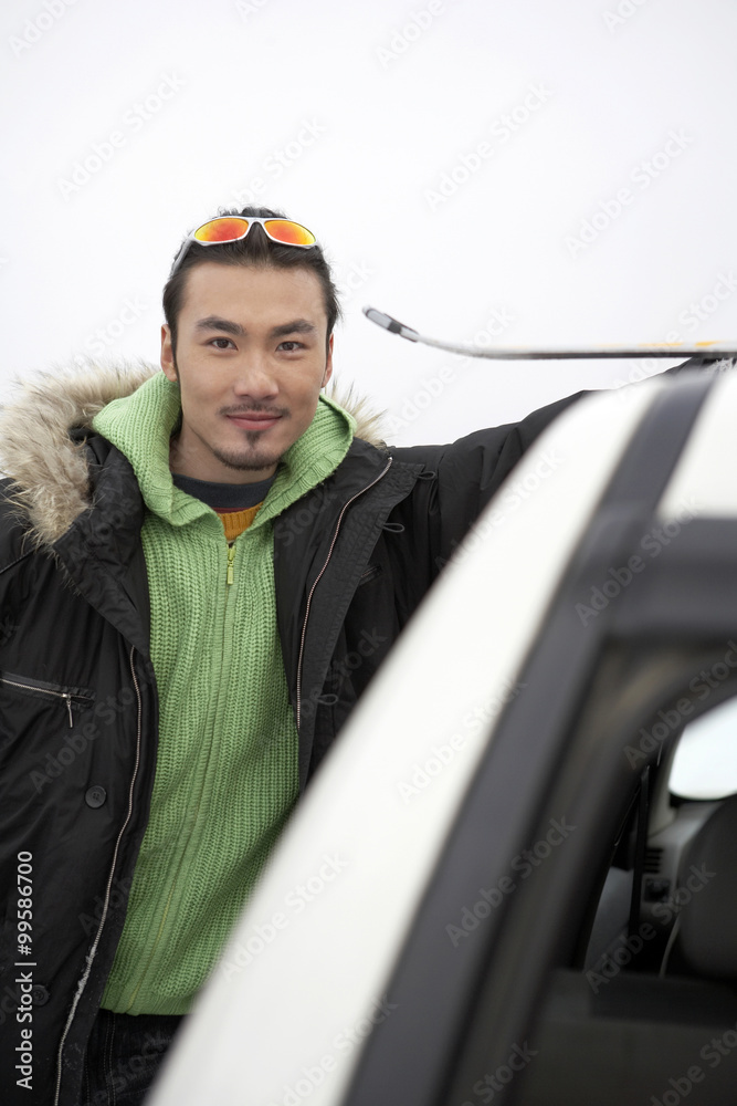 男子站在滑雪场上，靠在汽车上