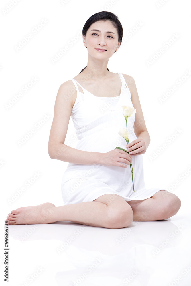 年轻孕妇盘腿坐着，手里拿着康乃馨