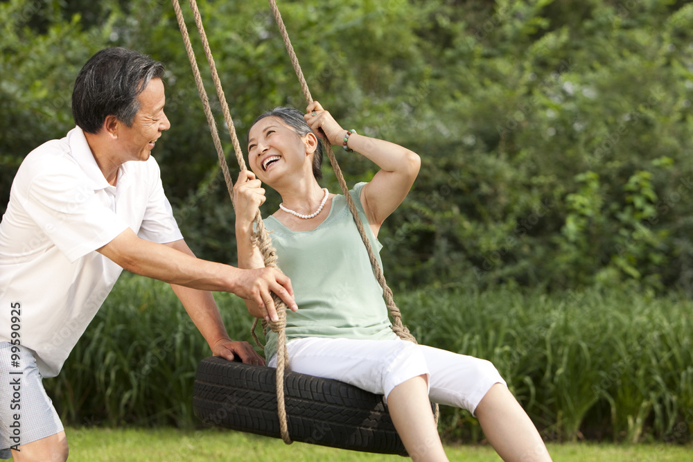 Cheerful senior couple playing on a swing