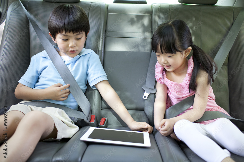 可爱的男孩和女孩在车里玩数字平板电脑