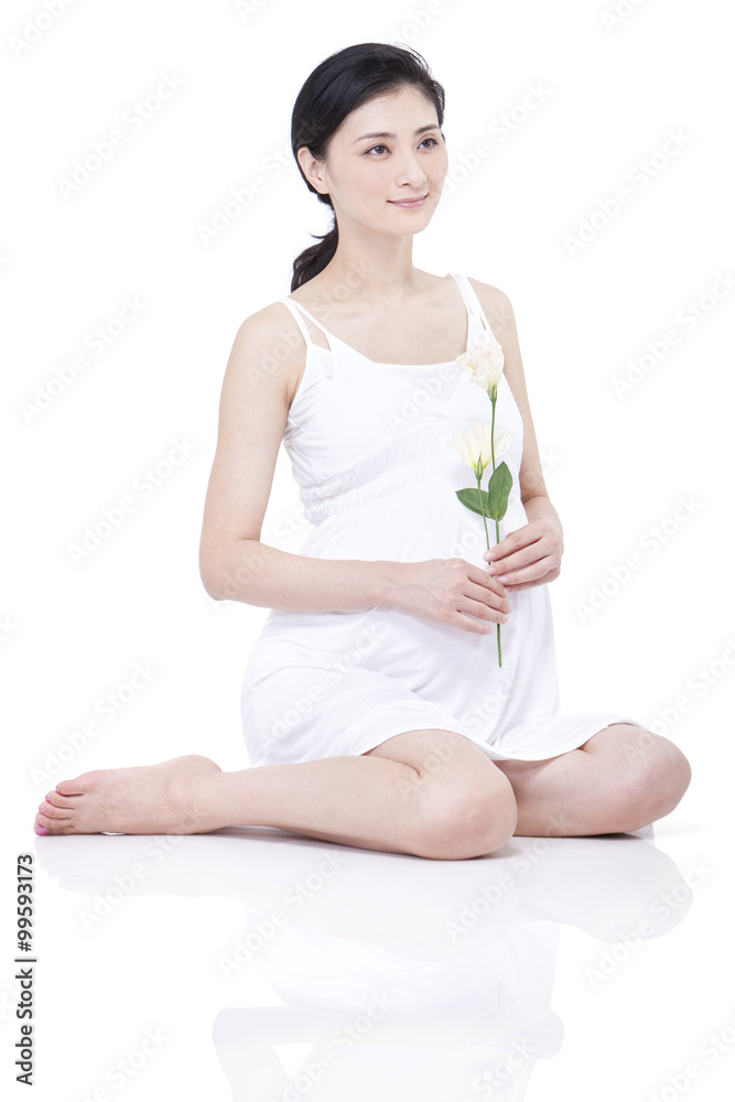 Young pregnant woman sitting cross-legged with carnation in hand