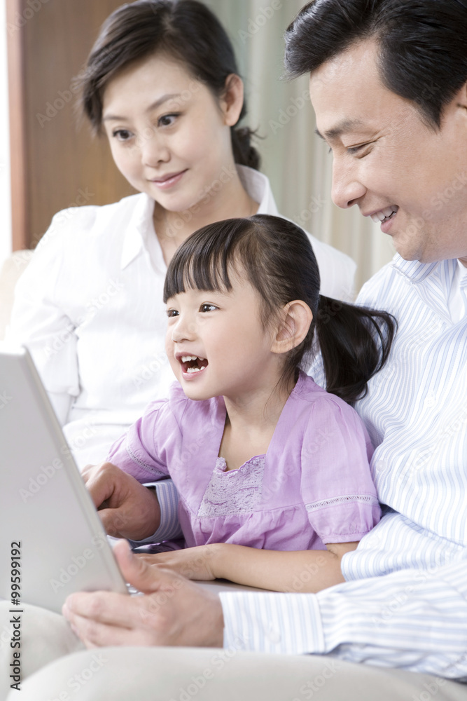 年轻夫妇和女儿看着沙发上的笔记本电脑
