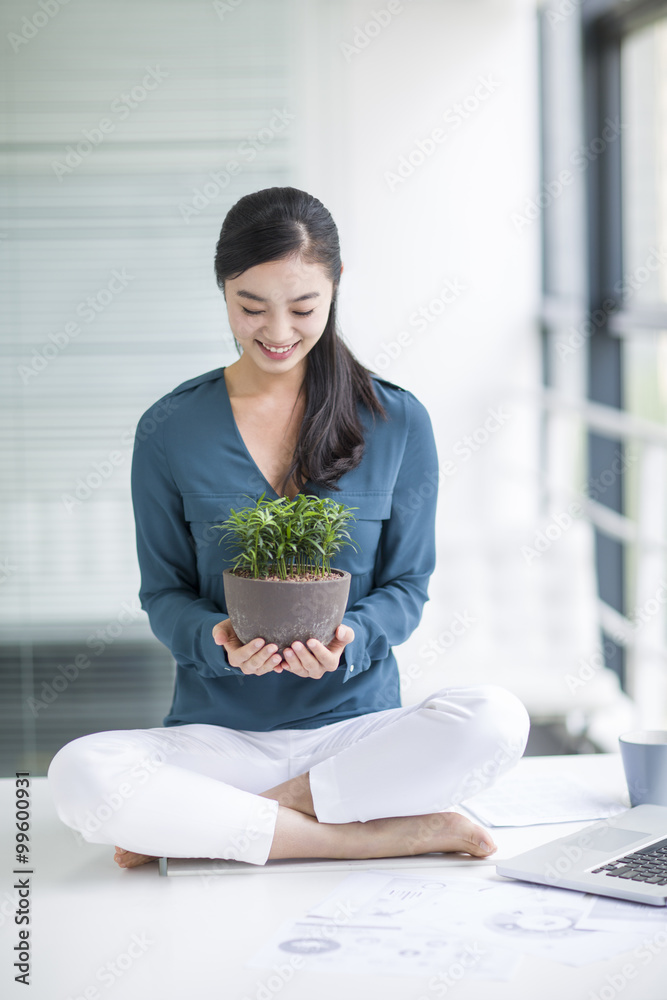 Young businesswoman sitting on office desk with a potted plant