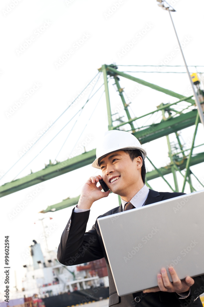 商人在船运港口使用笔记本电脑和手机