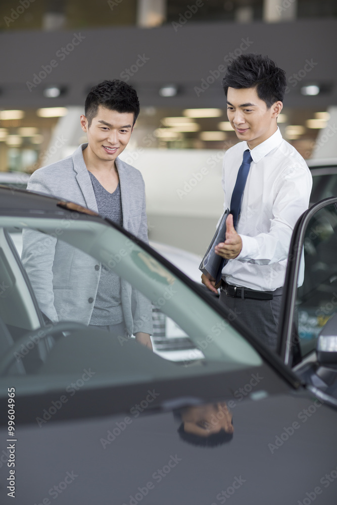 Young man choosing car in showroom
