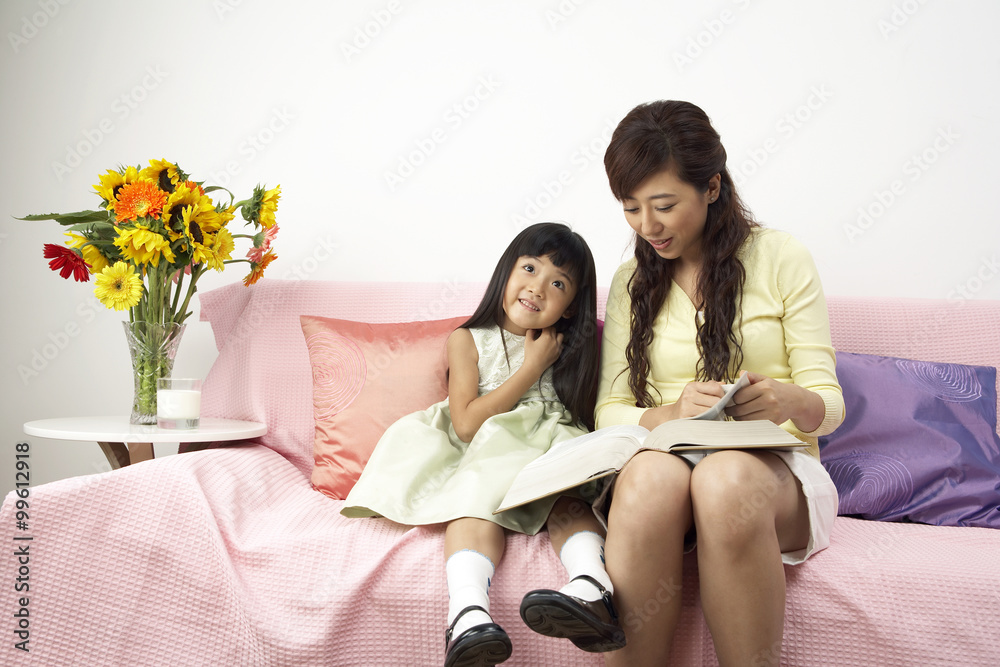 母亲和女儿在沙发上看书