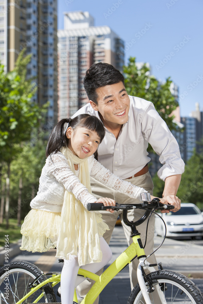 好心的年轻父亲在街上教女儿骑自行车