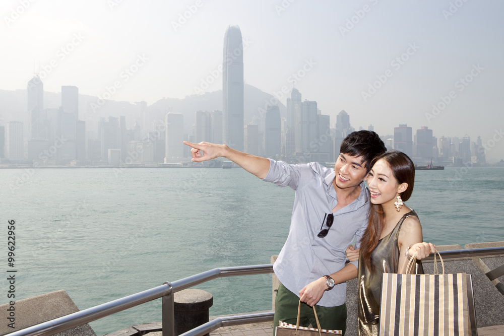 幸福的年轻夫妇带着购物袋欣赏香港维多利亚港的壮丽景色