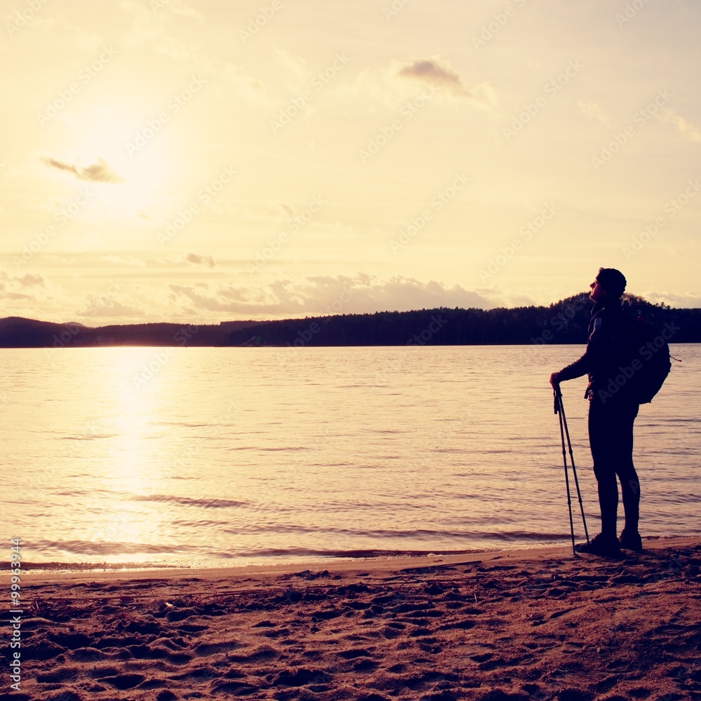 徒步旅行者穿着深色运动服，背着运动背包，站在海滩上，放松身心，享受阳光