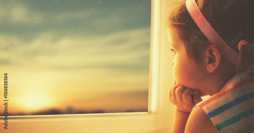 日落时，一个悲伤的小女孩看着窗外