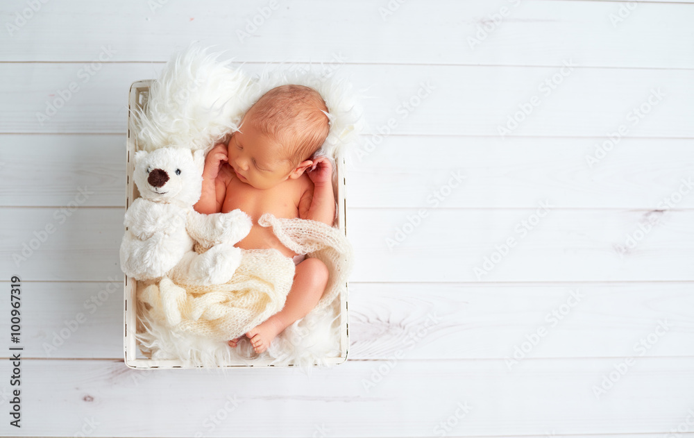 可爱的新生儿抱着玩具泰迪熊睡觉
