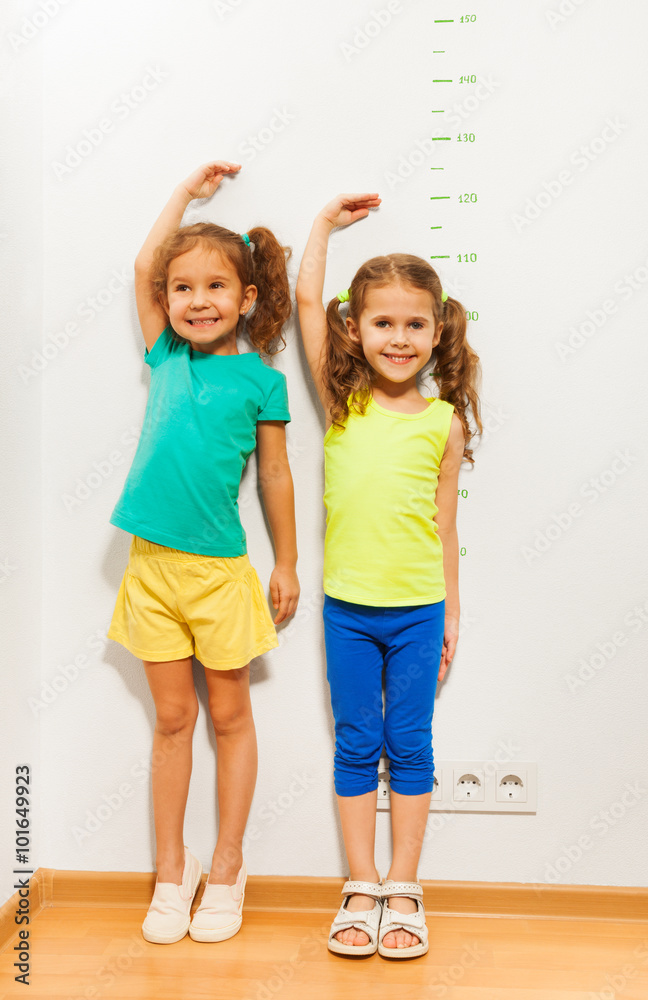 两个女孩在墙上的磅秤附近双手交叉