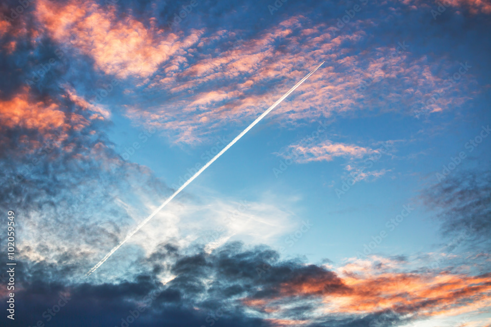 飞机在日落时戏剧性的云层中飞行并留下痕迹