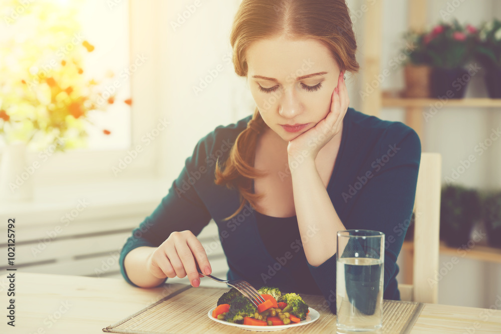 年轻悲伤的女人在家的厨房里吃蔬菜