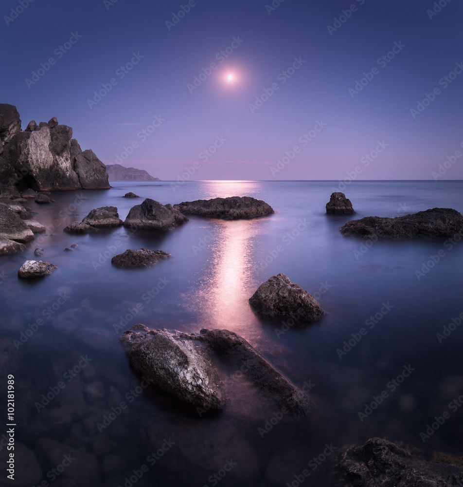Colorful seascape with moon and lunar path with rocks at night in summer. Mountain landscape at the 