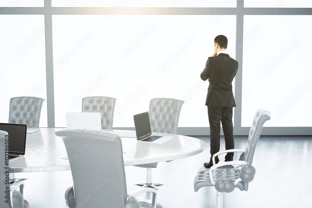 一个男人站在一个有桌子和椅子的会议室里