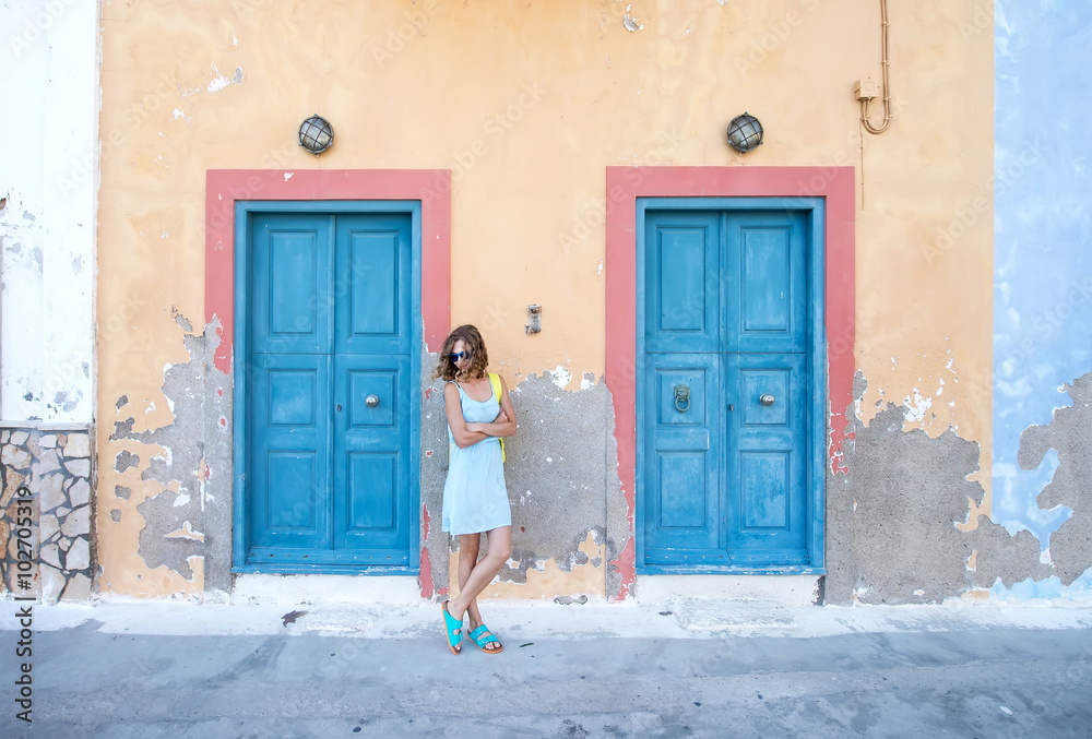 Yound blond woman at typical greek traditional town with colorful buildings on Kastelorizo Island, G