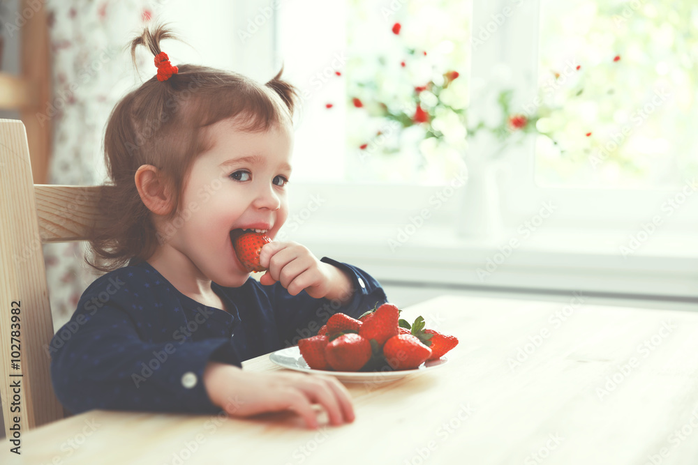 快乐的小女孩在夏季家庭厨房吃草莓