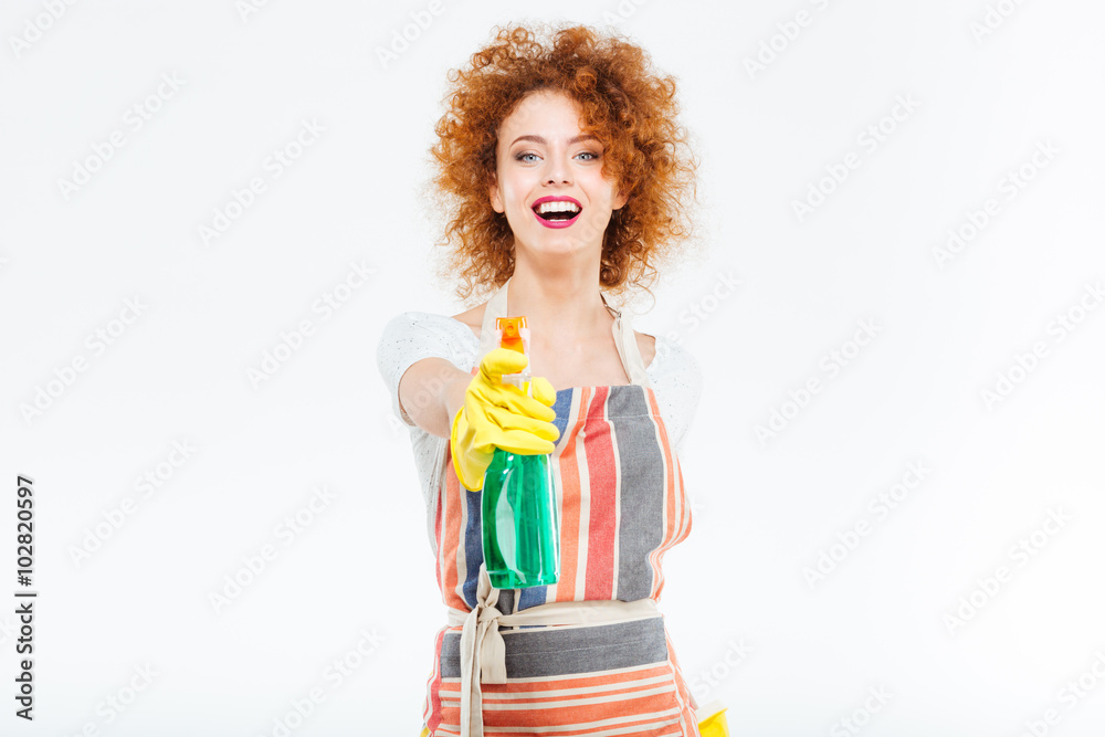 Cheerful woman in yellow gloves holding spray with liquid detergent