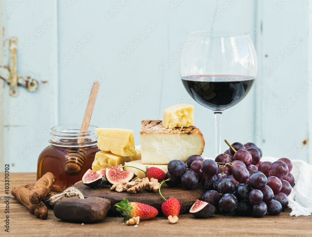 一杯红酒、奶酪板、葡萄、无花果、草莓、蜂蜜和面包棒放在乡村的木头上