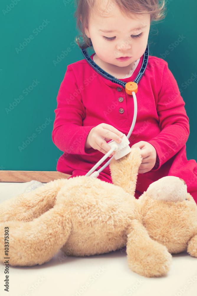 蹒跚学步的女孩用听诊器照顾她的泰迪熊