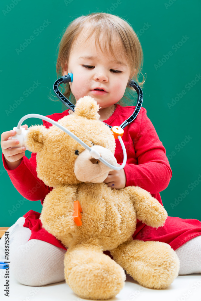 蹒跚学步的女孩用听诊器照顾她的泰迪熊