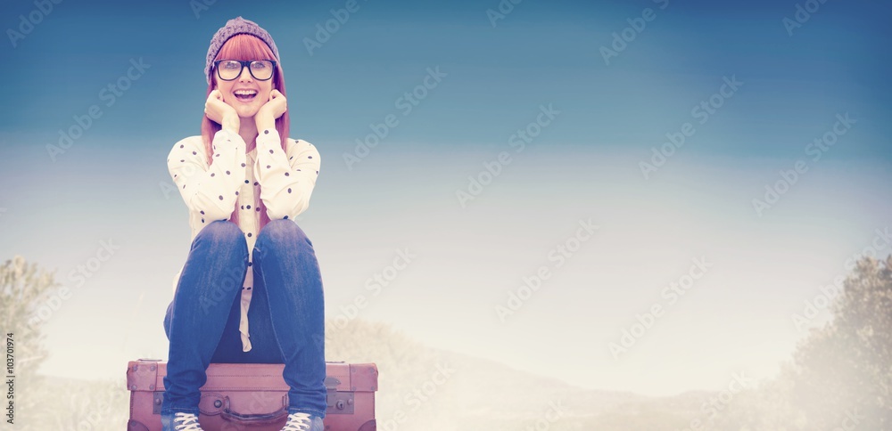 微笑的时髦女人坐在行李箱上的合成图像