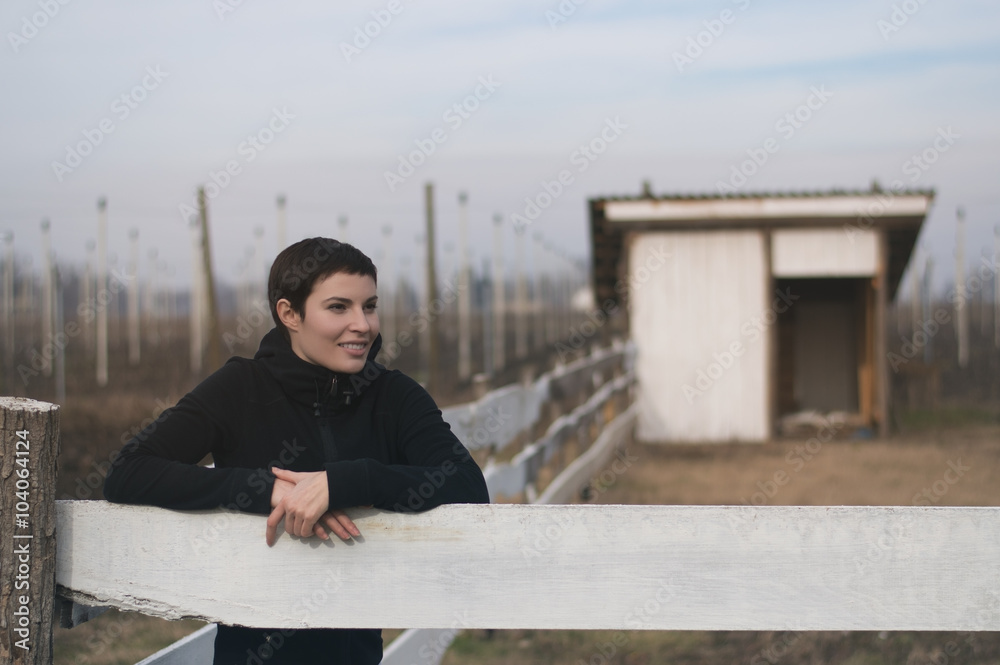 Young woman is standing by a fence on a ranch