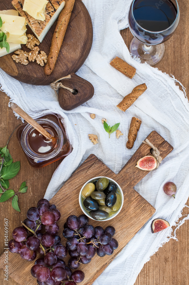 一杯红酒、奶酪板、葡萄、核桃、橄榄、蜂蜜和面包棒放在乡村的木制ta上