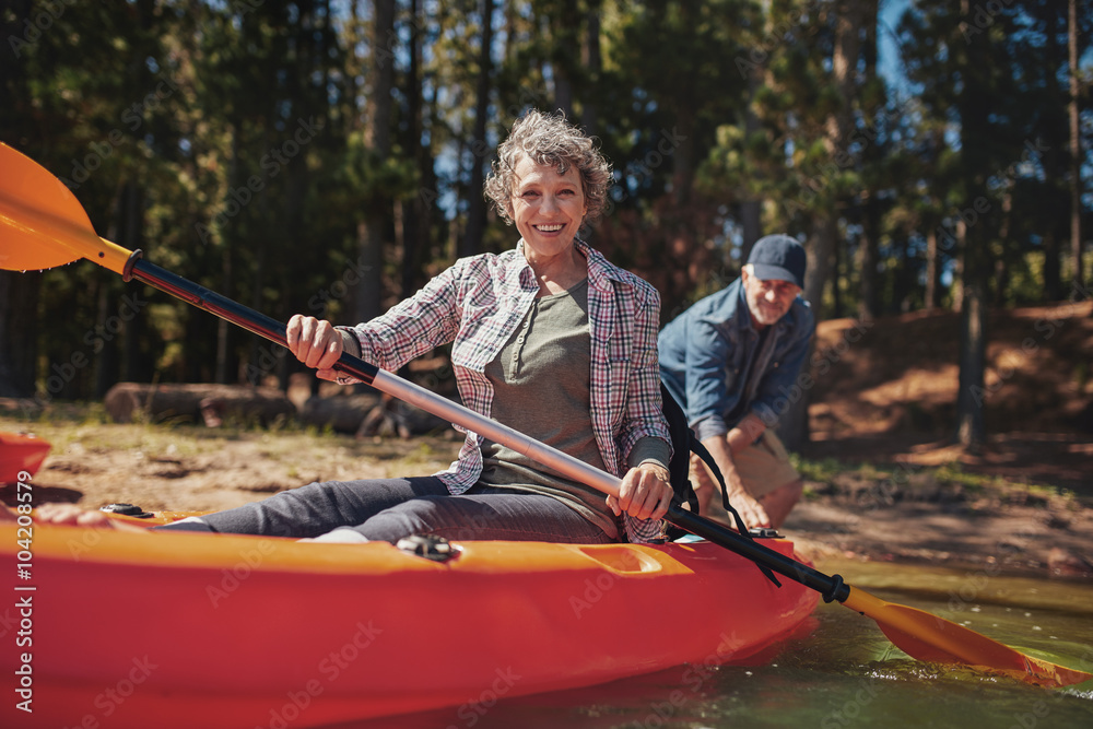 快乐的老年妇女在湖边的皮划艇上