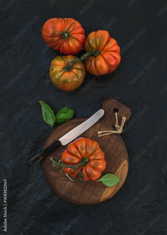 在黑色石头背景下的乡村木板上，新鲜成熟的发际番茄和罗勒叶。