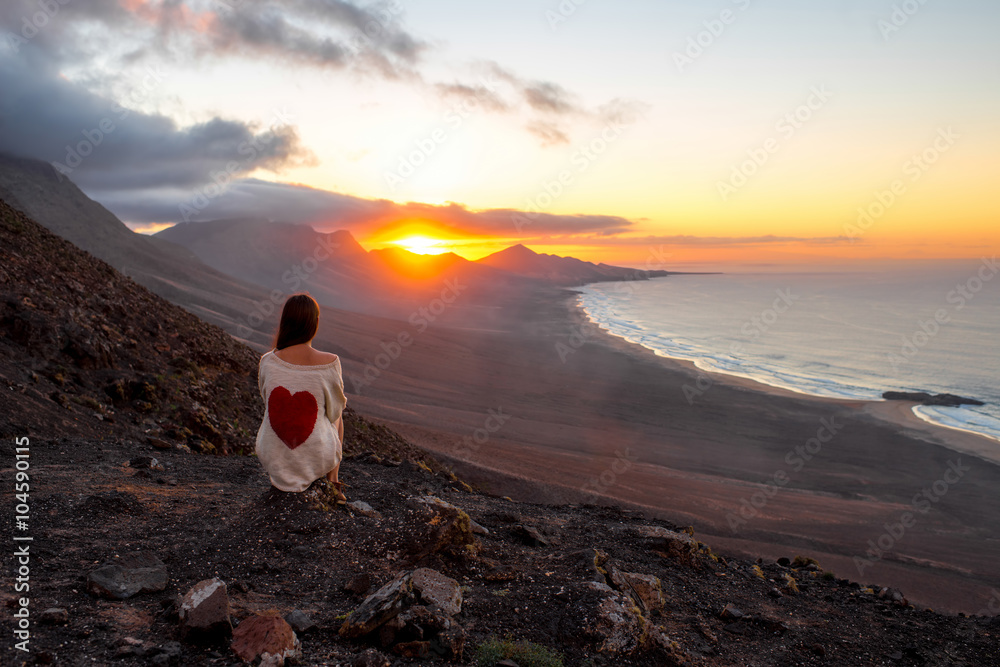 Young woman enjoying beautiful sunset sitting on the mountain with great view on Cofete coastline on