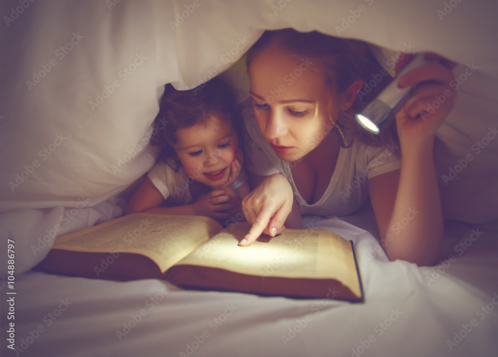 家庭睡前阅读。妈妈和孩子用手电筒看书