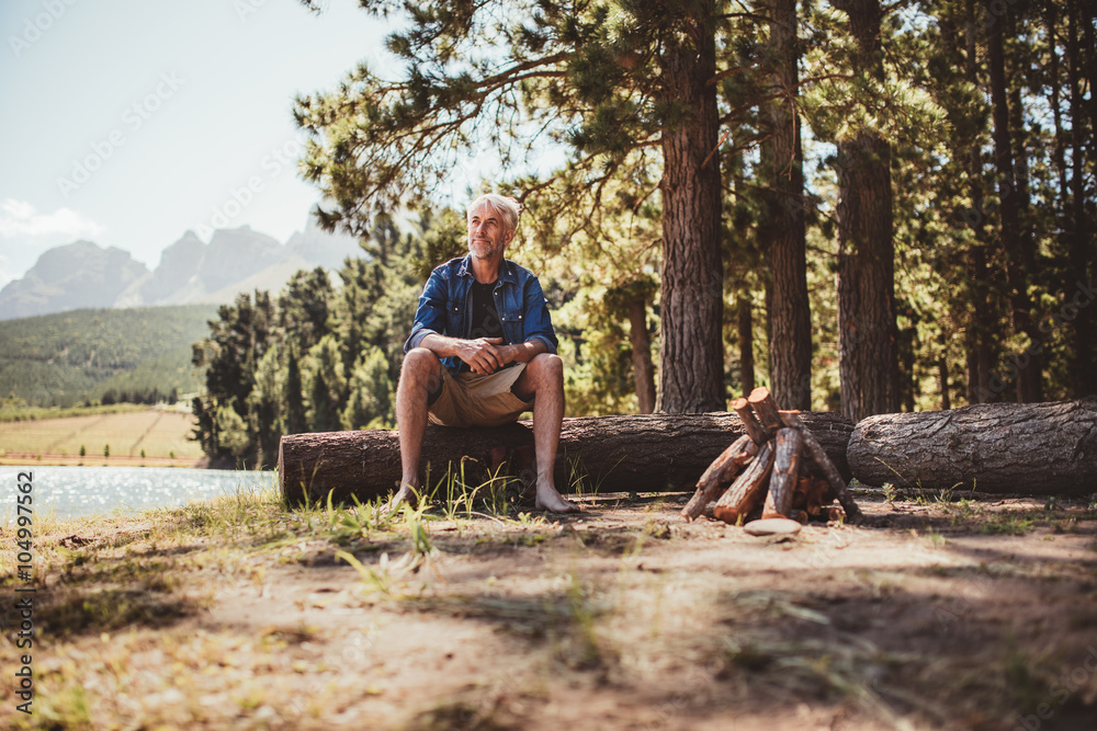 一个成熟的男人坐在木头上凝视着湖面