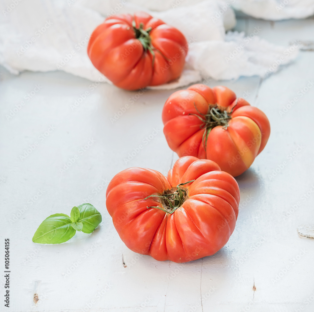 浅蓝色木质背景上新鲜成熟的发际番茄和罗勒叶。