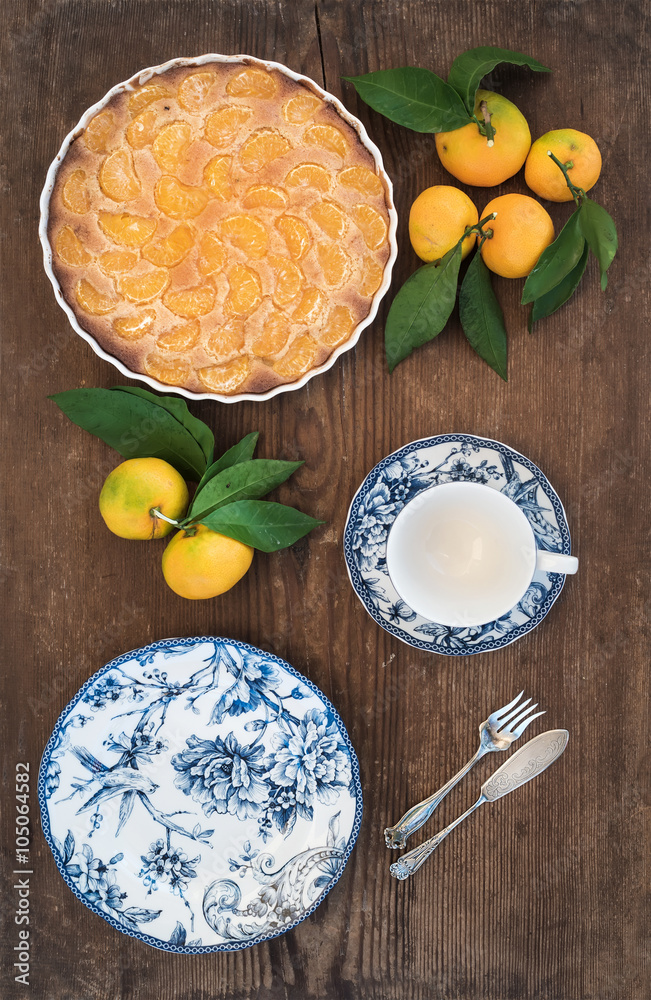Homemade tangerine pie, fresh fruit and porcelain dinnerware over rustic wooden background