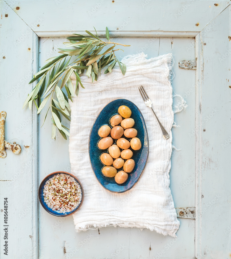 绿色大橄榄，装在乡村陶瓷盘中，树枝和香料放在厨房毛巾上，浅蓝色
