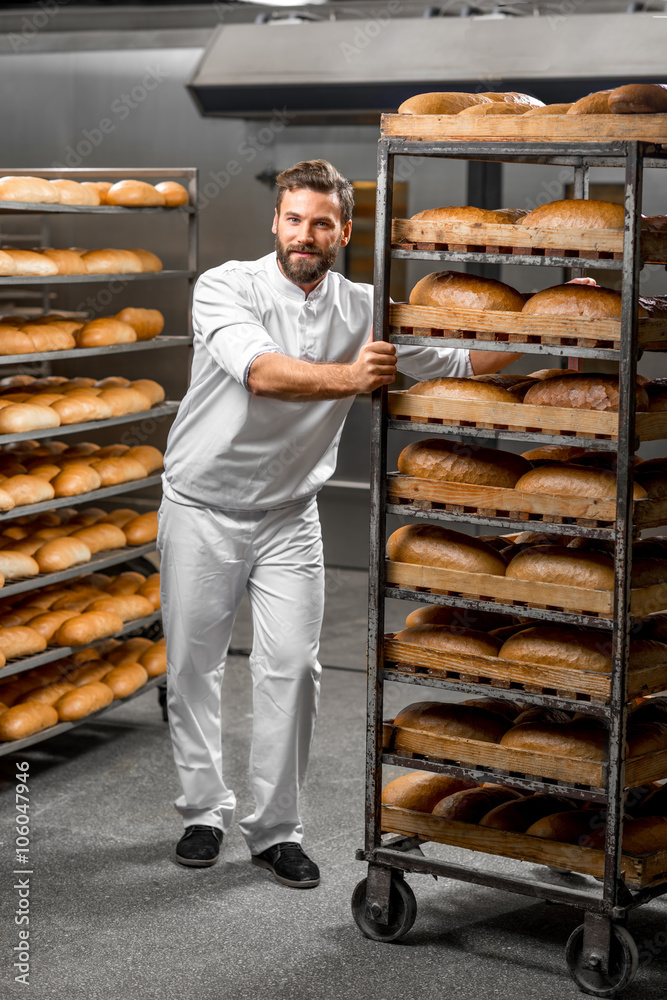 Handsome worker in uniform carrying shelves with bread at the bakery manufacturing