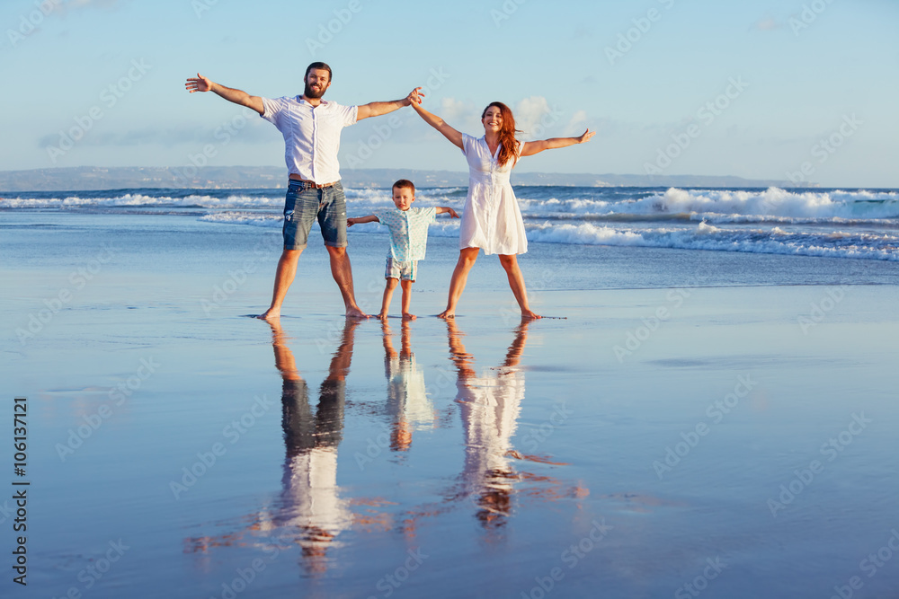 幸福的家庭——父亲、母亲、小儿子沿着日落的边缘在黑沙滩上冲浪，玩得很开心