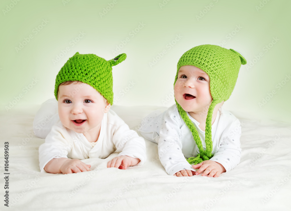 两个可爱的婴儿戴着青蛙帽躺在间谍毯上