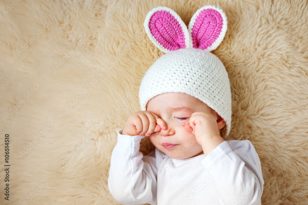 一岁婴儿戴着兔子帽躺在羊羔毛上