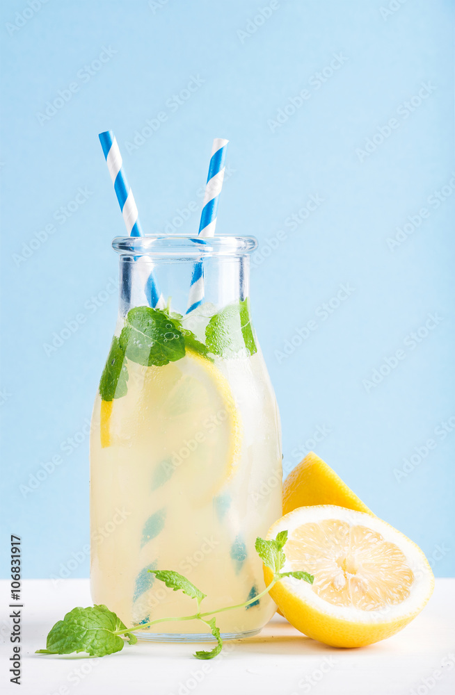 一瓶自制柠檬水，配薄荷、冰块、柠檬、纸吸管和淡蓝色背景