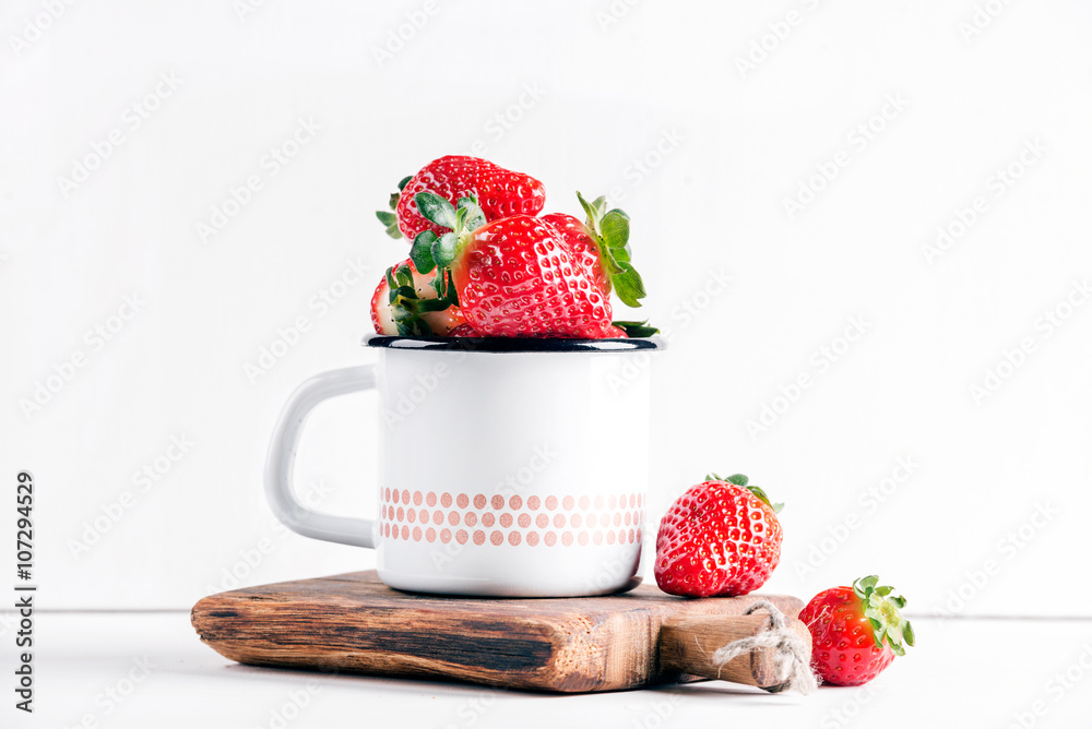 新鲜成熟的红色草莓，装在乡村风格的搪瓷马克杯上，装在白色背景的乡村木板上