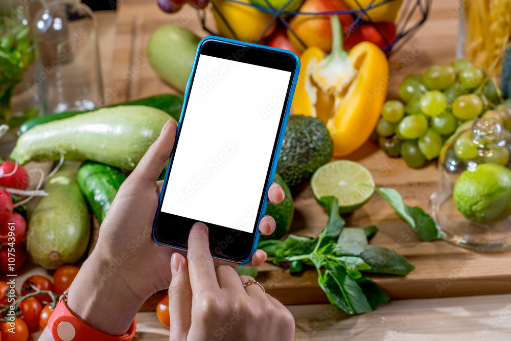 女性手持智能手机，白色屏幕，背景是五颜六色的水果