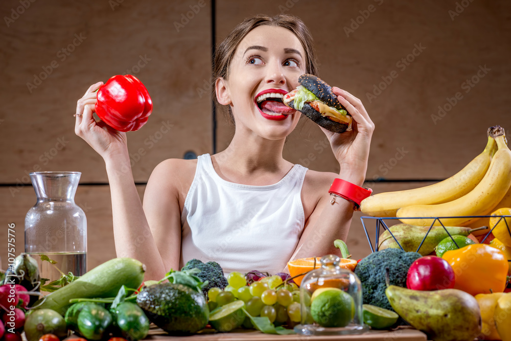 年轻的运动女性在充满水果的餐桌上选择汉堡和健康但无味的食物